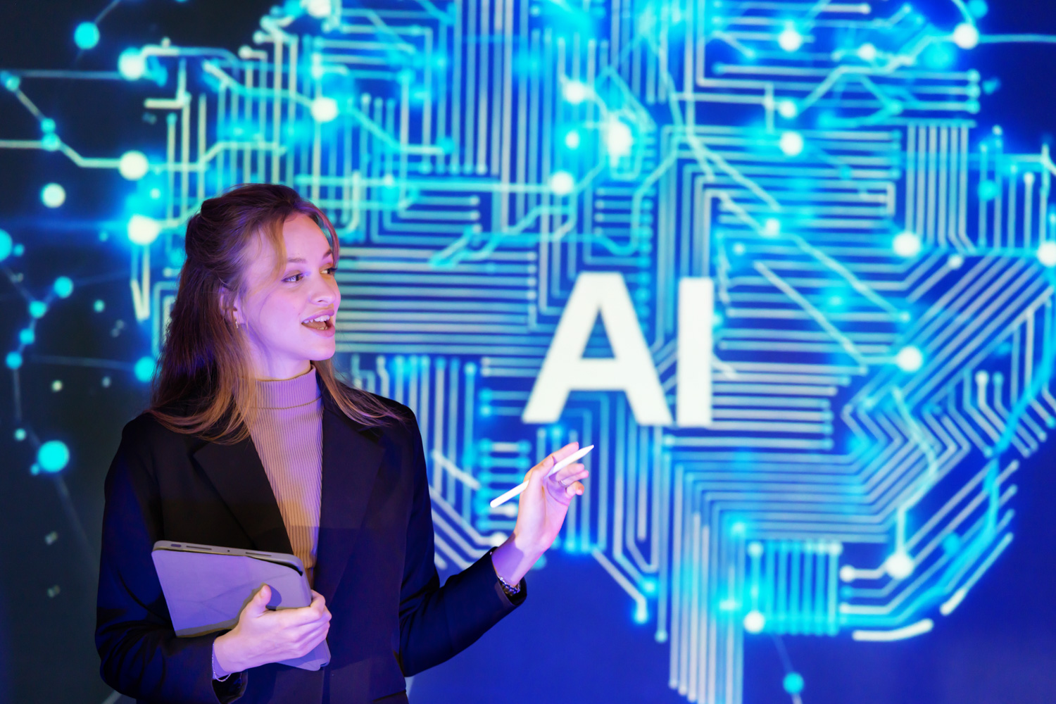 A woman holding a tablet and stylus gestures toward a large illuminated "AI" display on a digital circuit board background.