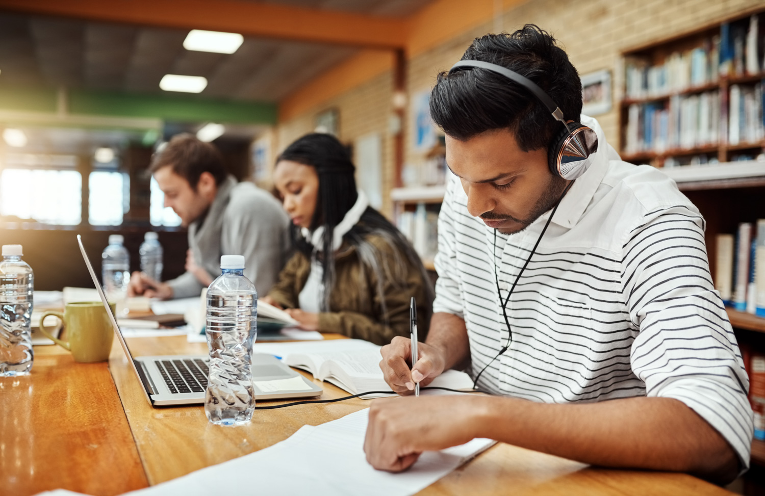 Student working at a desk, preparing notes while two other students do the same in the background.