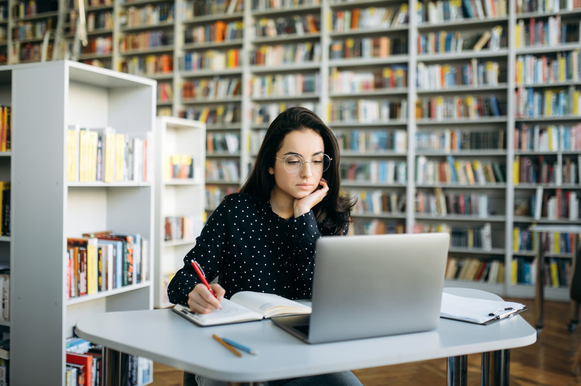 A focused woman studies at a library desk with a laptop.