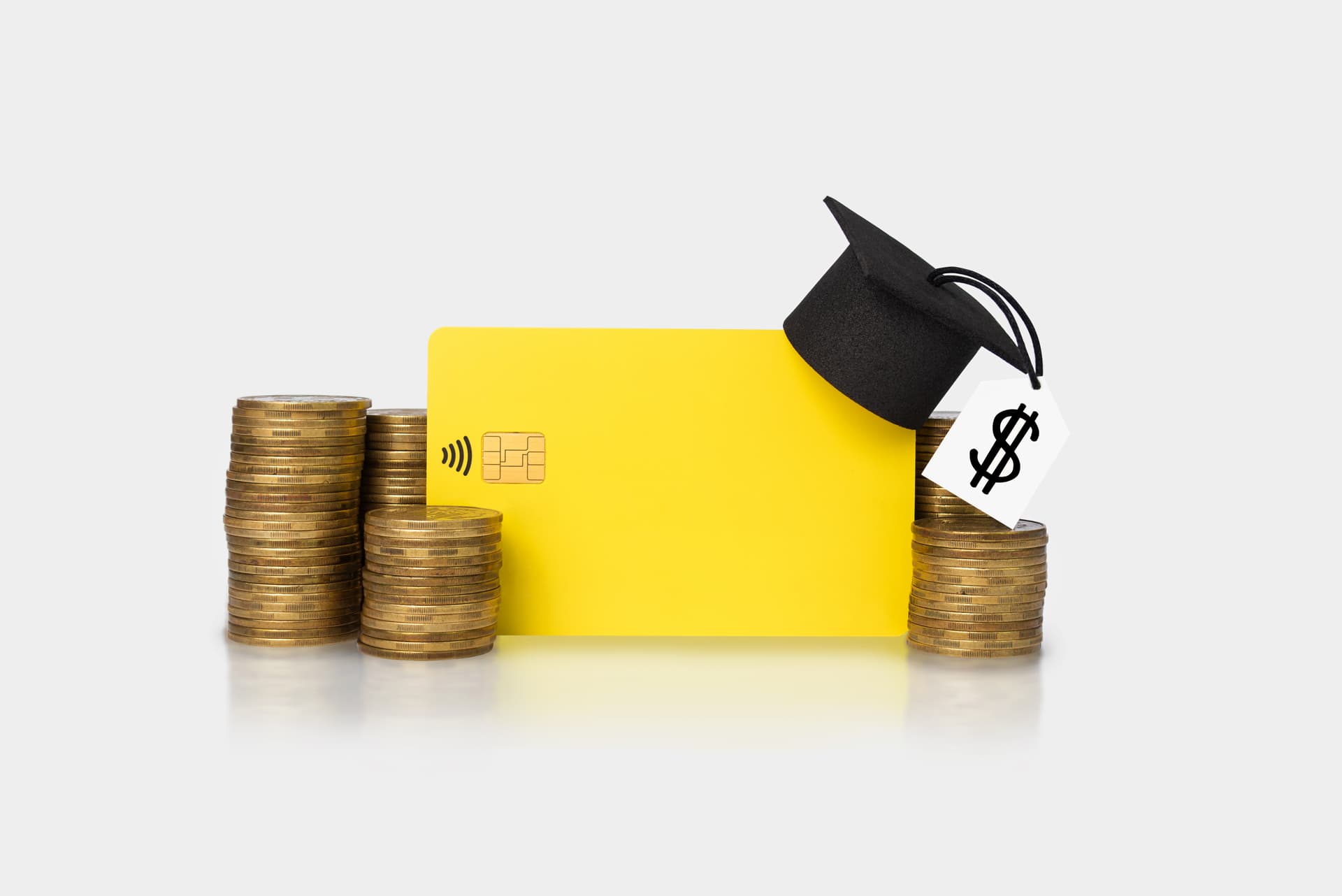 Stacks of gold coins around a yellow bank card with a graduation cap on top.