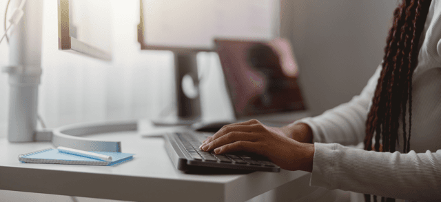 Someone typing at a keyboard though their full body is not in focus, only the arms are.
