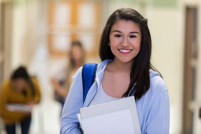 Student carrying backpack and school supplies.
