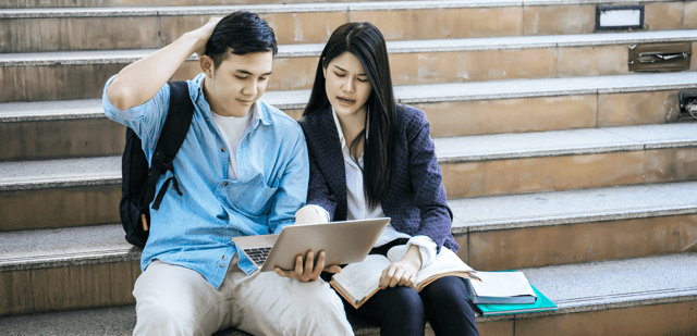 Two individuals sitting on the last few seps of a staircase, looking at a laptop together