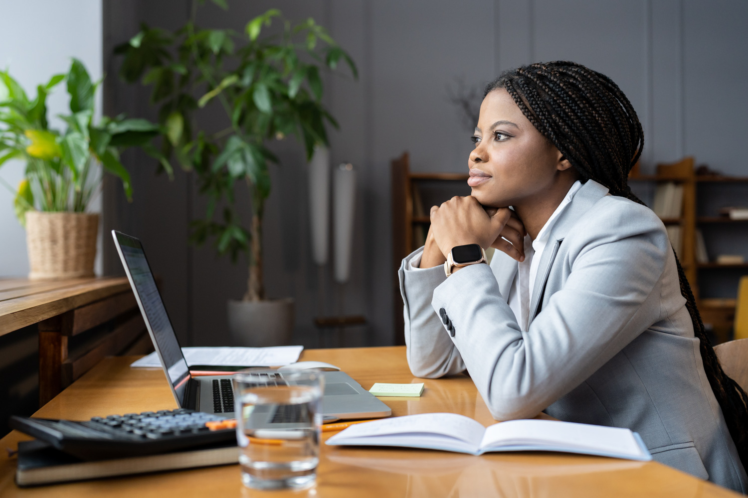 A student sits at a desk with her laptop and notes, looking out into the distance.